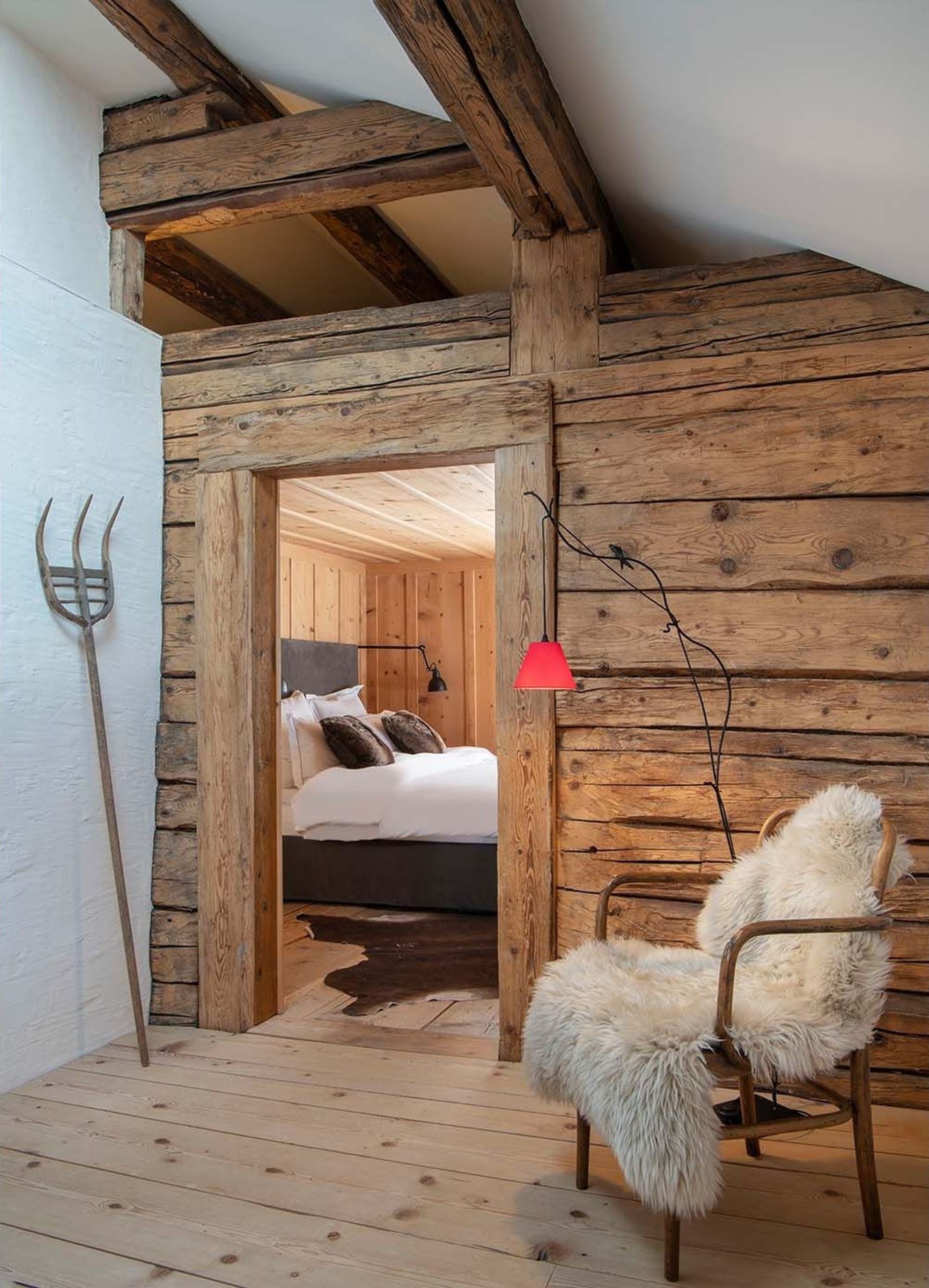 Hallway with reclaimed timber, fur chair and view into the bedroom – Historic conversion in Fidaz