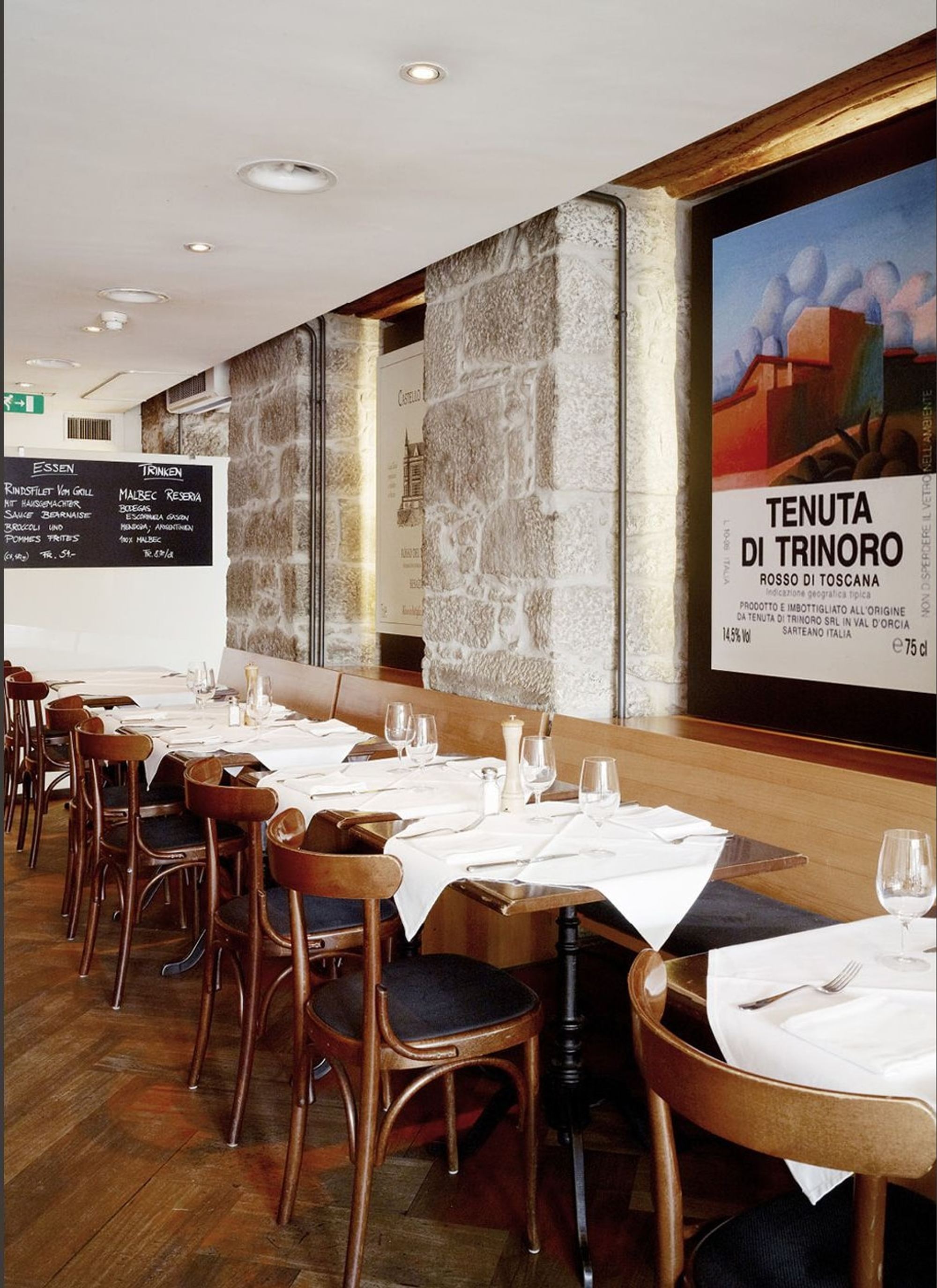 Row of tables in front of a stone wall and poster – Interiors and landscape, Zürich