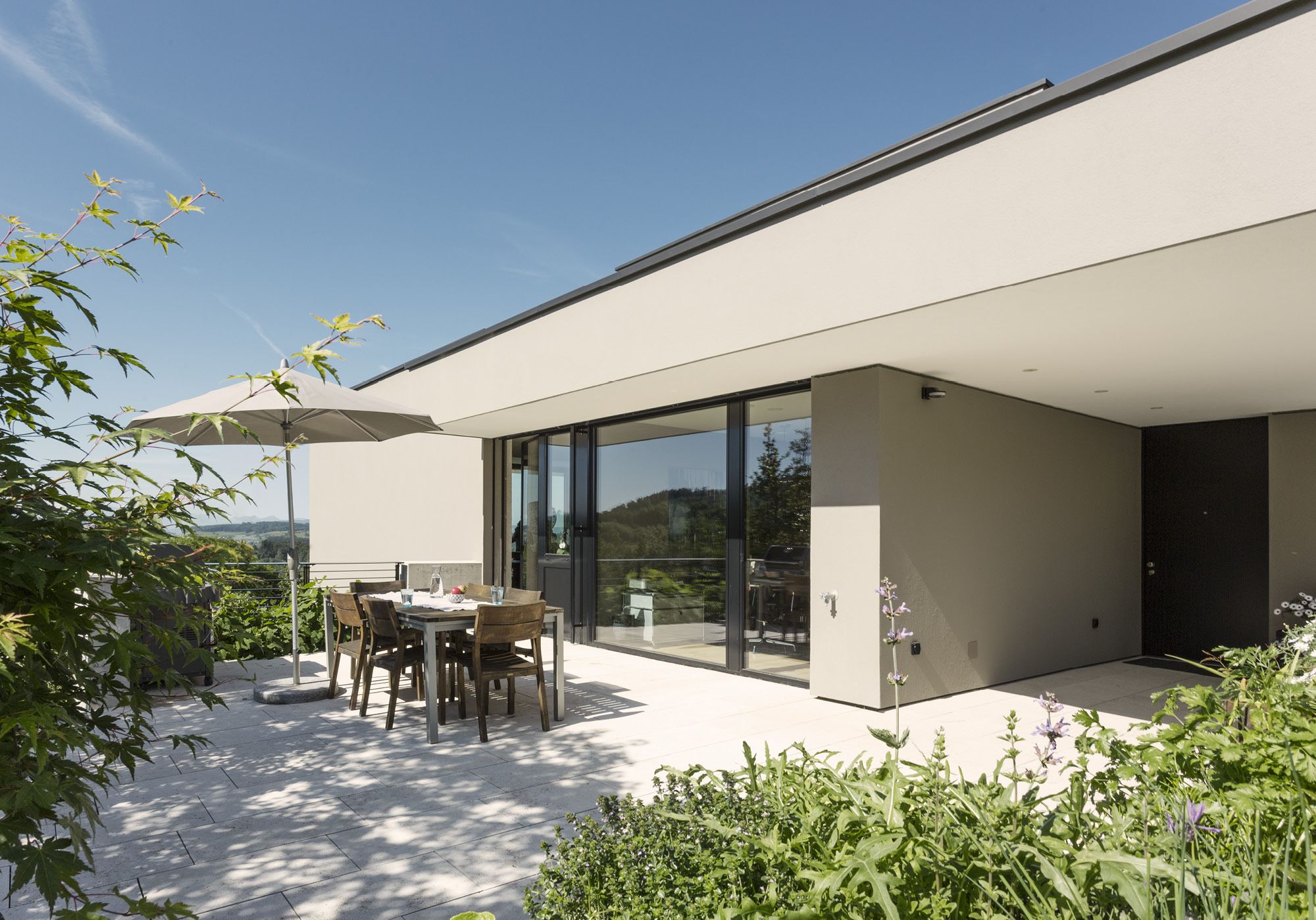 Seating area with dining table and parasol by the glass front – Single-family house in Uitikon