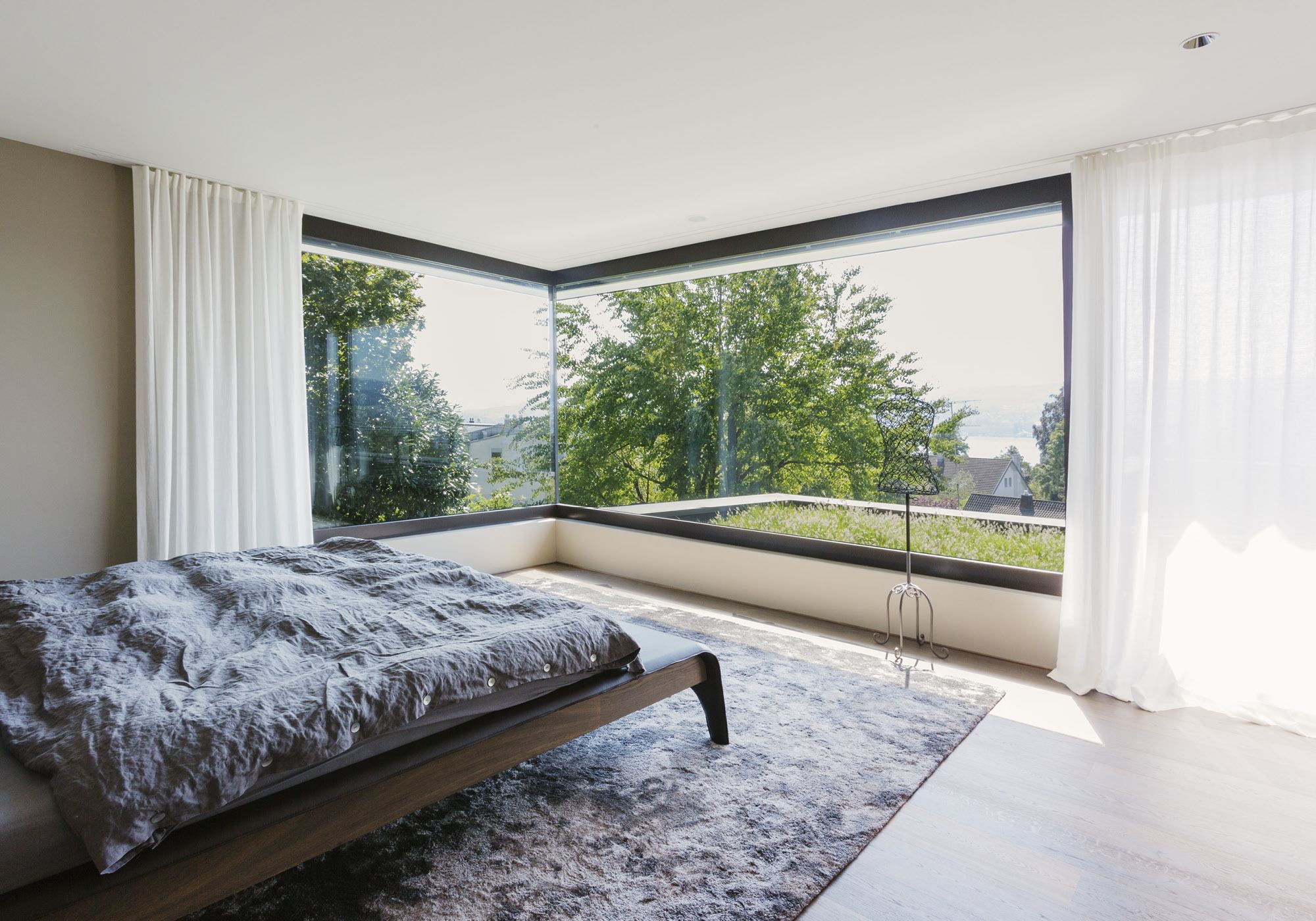Bedroom with corner glazing and green view – Single-family house in Meilen