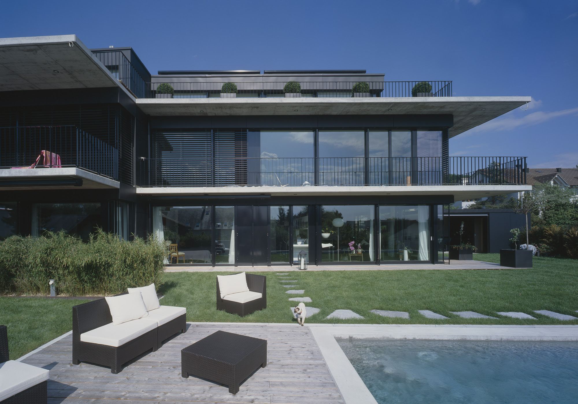 Lounge furniture by the pool in front of the glass facade – Apartment building in Uitikon
