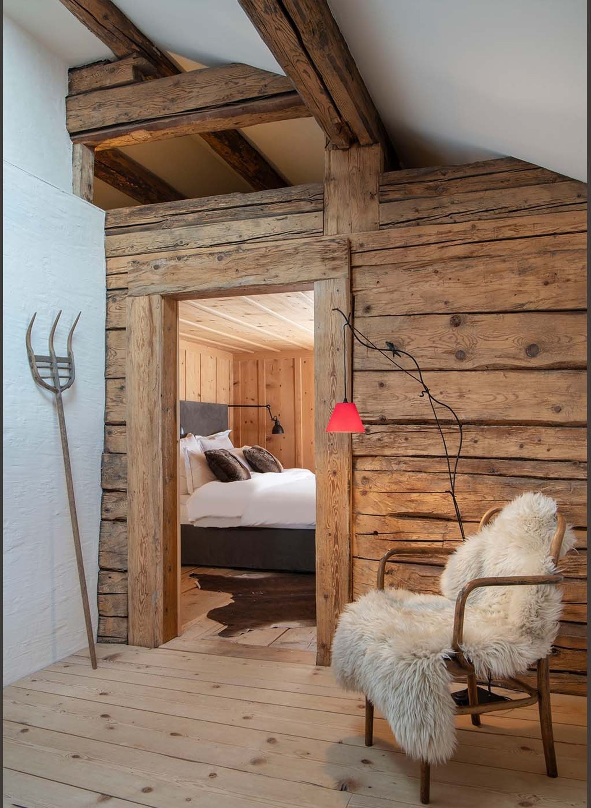 Hallway with reclaimed timber, fur chair and view into the bedroom – Historic conversion in Fidaz