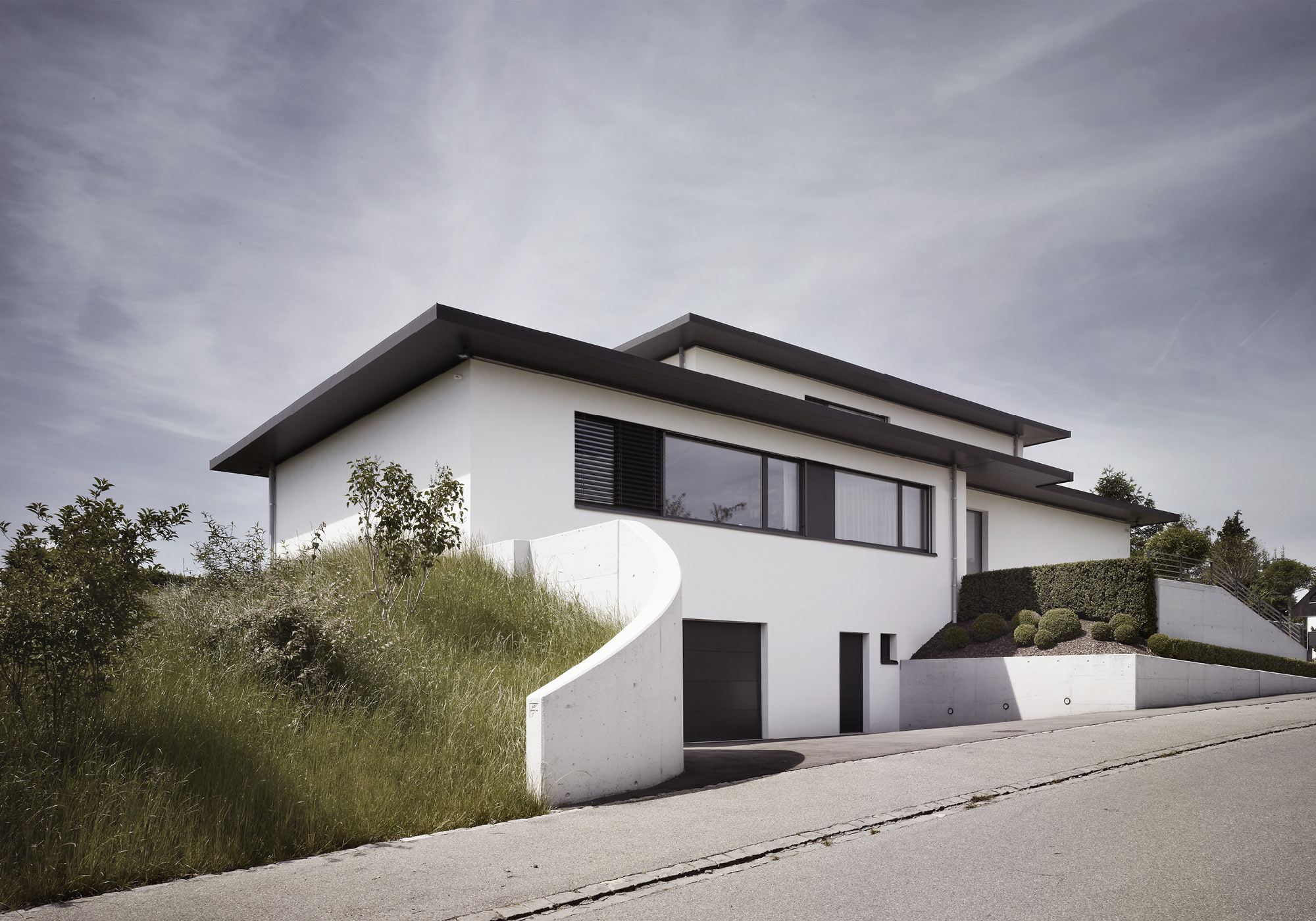 Curved wall on the slope in front of the house – Single-family house in Russikon