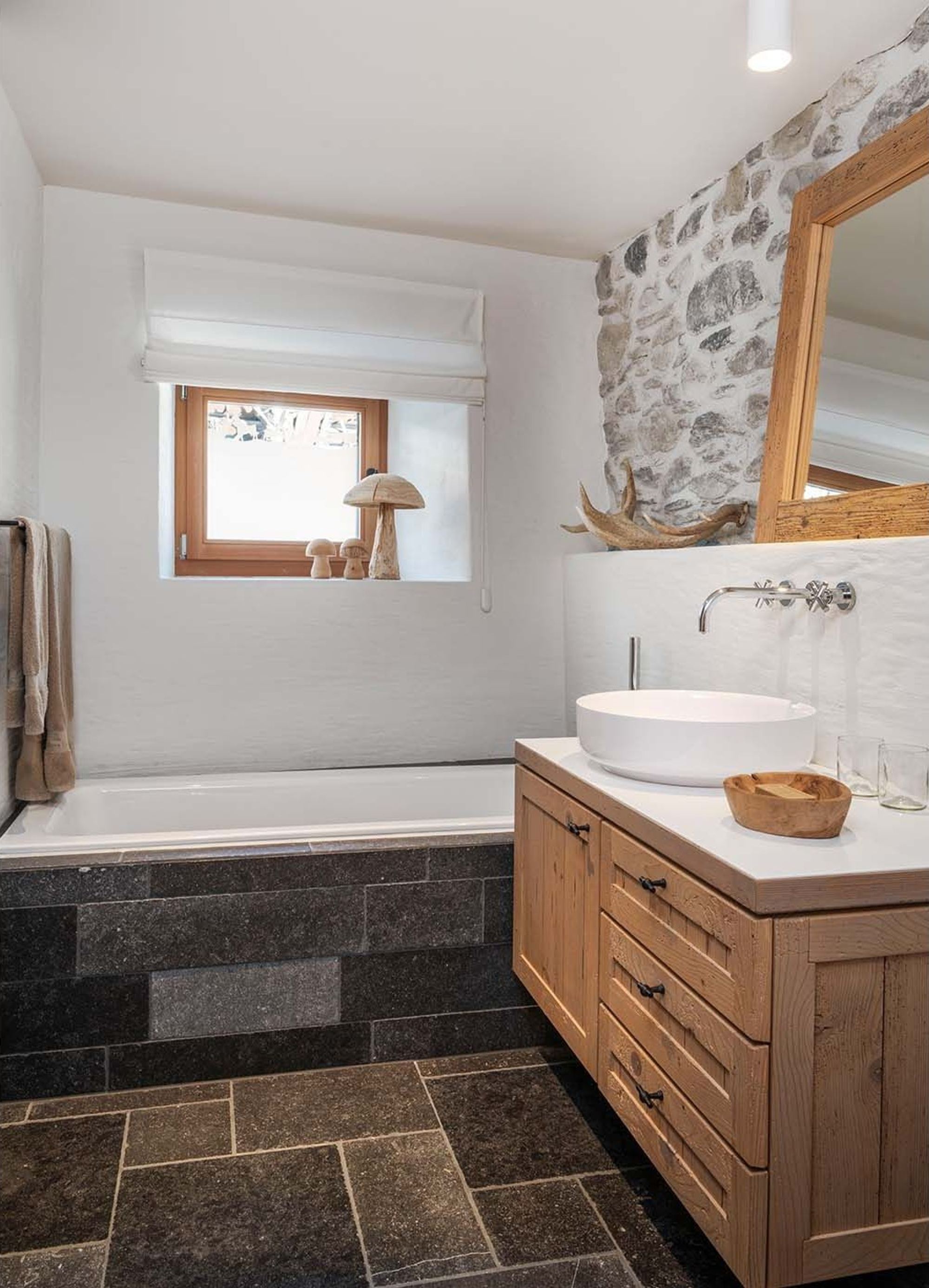 Bathroom with bathtub, timber vanity and stone wall – Historic conversion in Fidaz