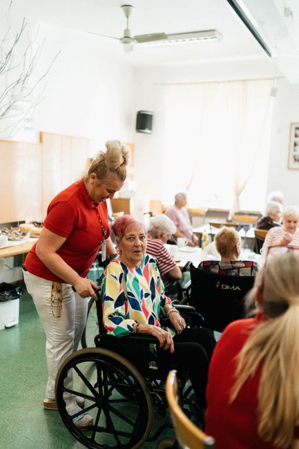 Sveikatos priežiūros darbuotoja padeda vyresniam žmogui bendruomenės centre