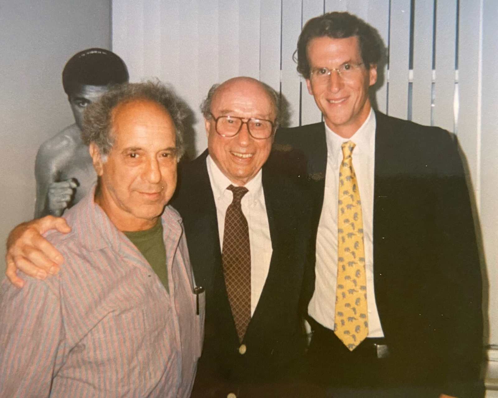 Peter MacGill in his office with artists Robert Frank and Harry Callahan in front of Muhammad Ali cutout, 1990s. The Getty Research Institute. 