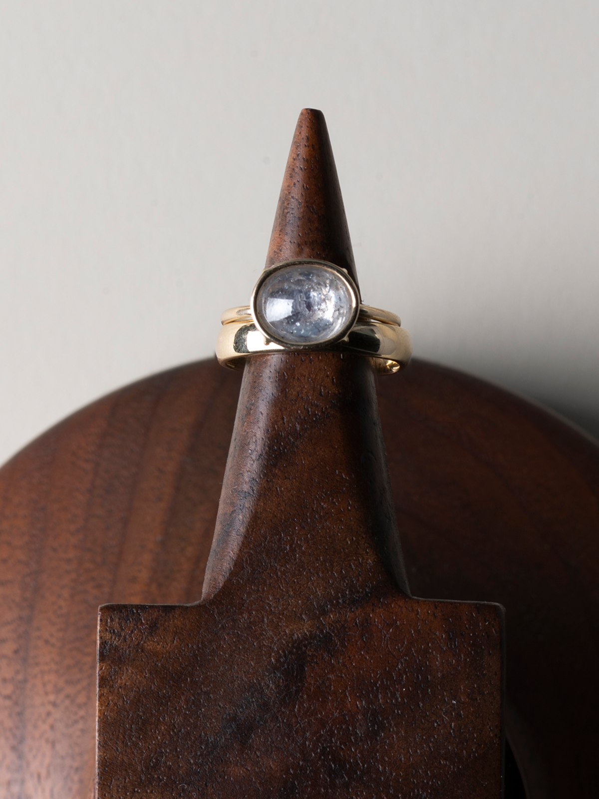 Gold ring with an oval stone, displayed on a wooden ring cone stand