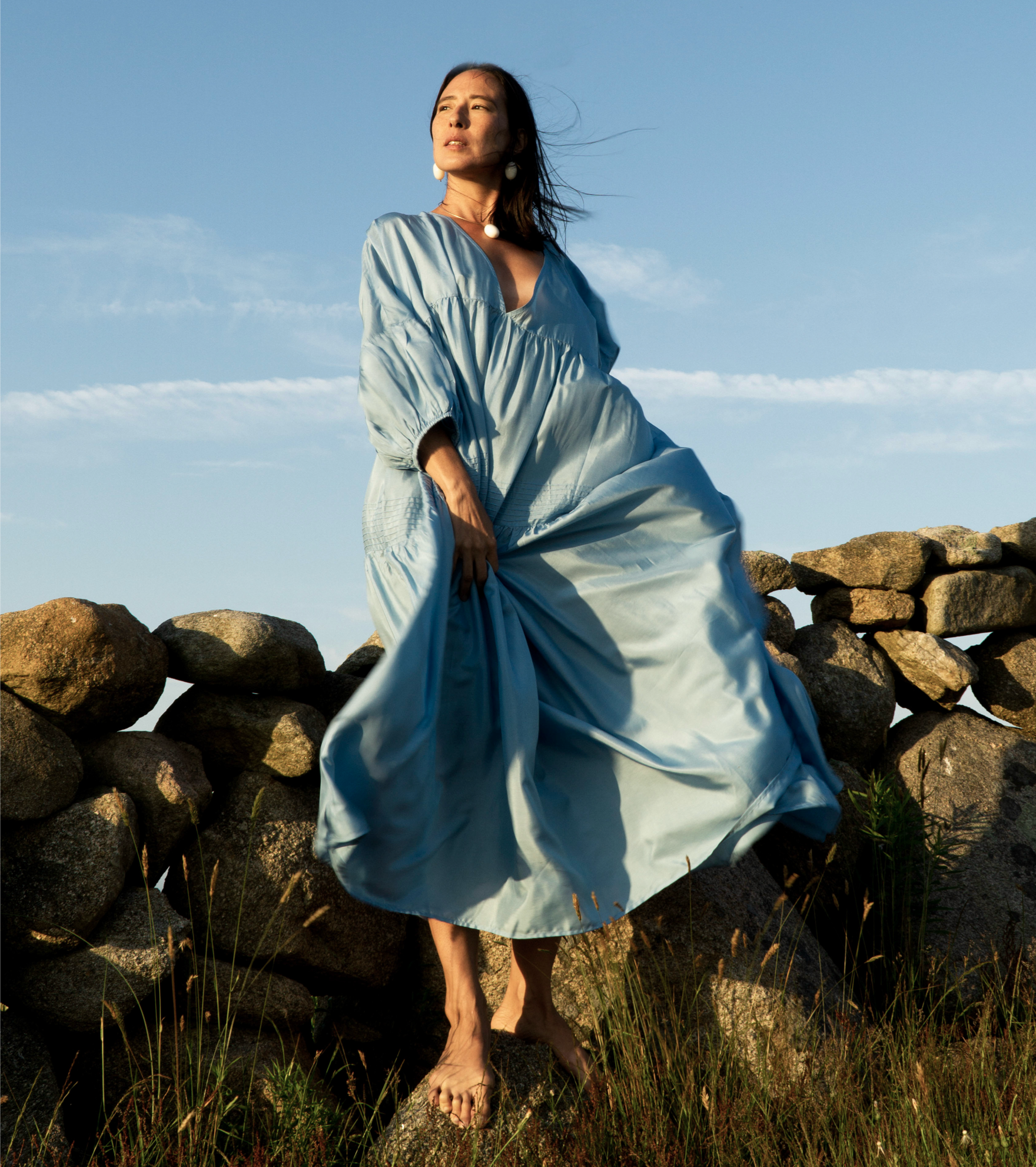 Woman standing on a large stone, in front of a wall of loose stones