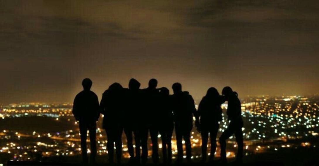 Silhouettes of a group of people overlooking a city lit up at night.