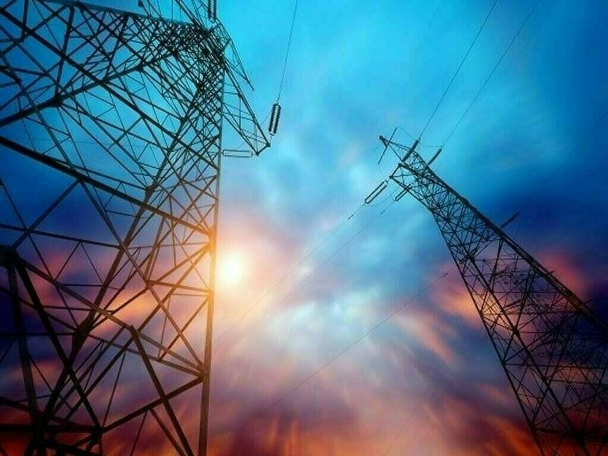 Two power transmission towers silhouetted against a vibrant blue and orange sky with a sunburst.