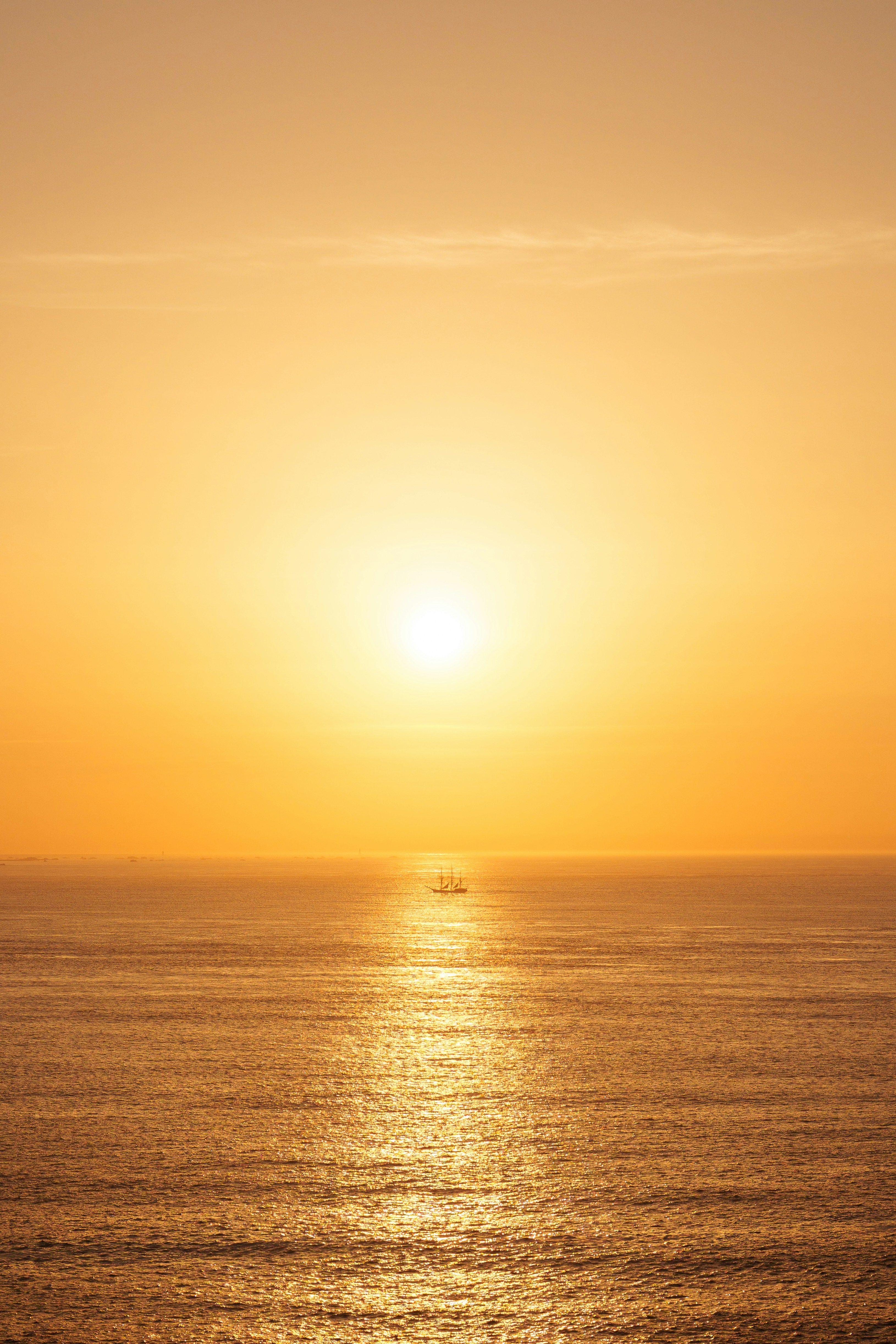 Golden sunset over the ocean with a tall ship in the distance.