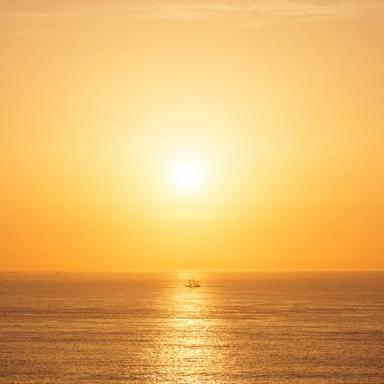 Golden sunset over the ocean with a tall ship in the distance.