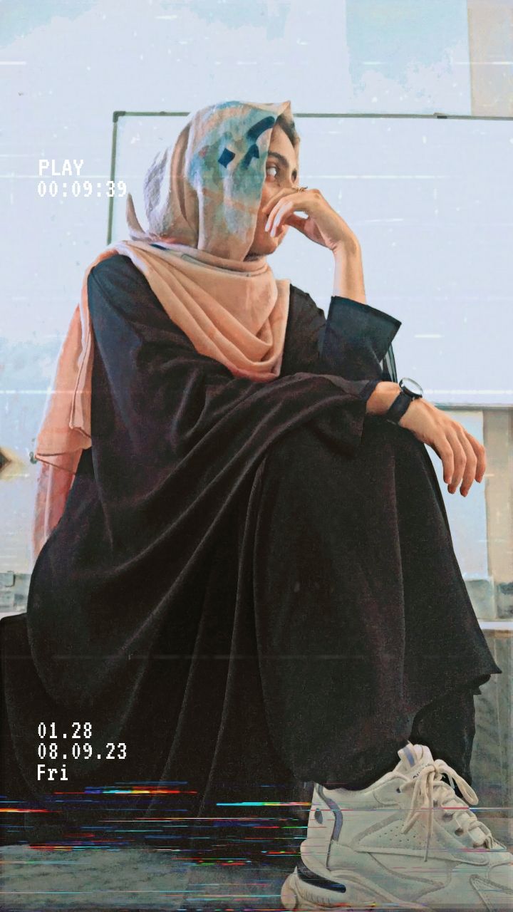 A person in a black abaya and peach hijab with blue accents, sitting thoughtfully with white sneakers, overlaid with a retro VHS filter.