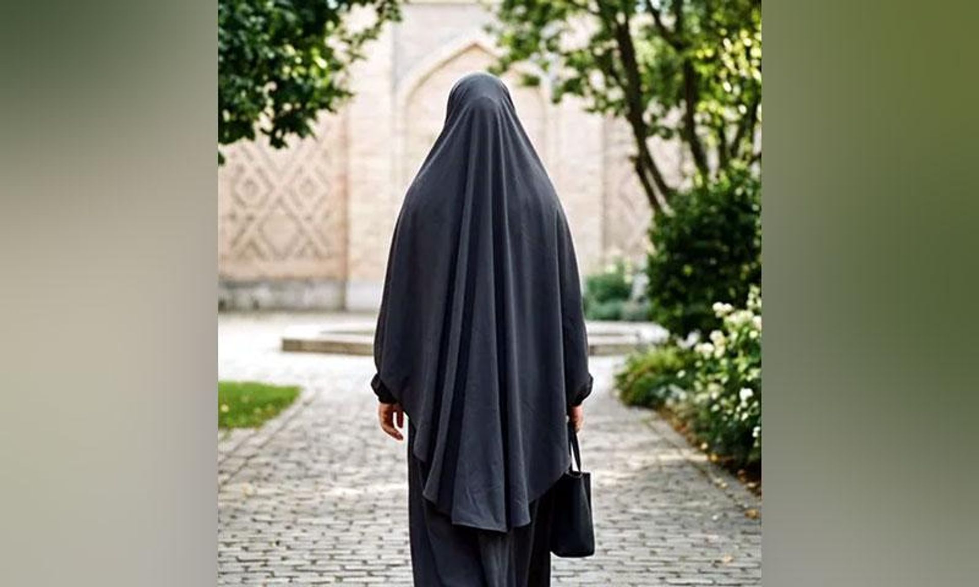 Back view of a person in a black full-body covering walking on a paved path.