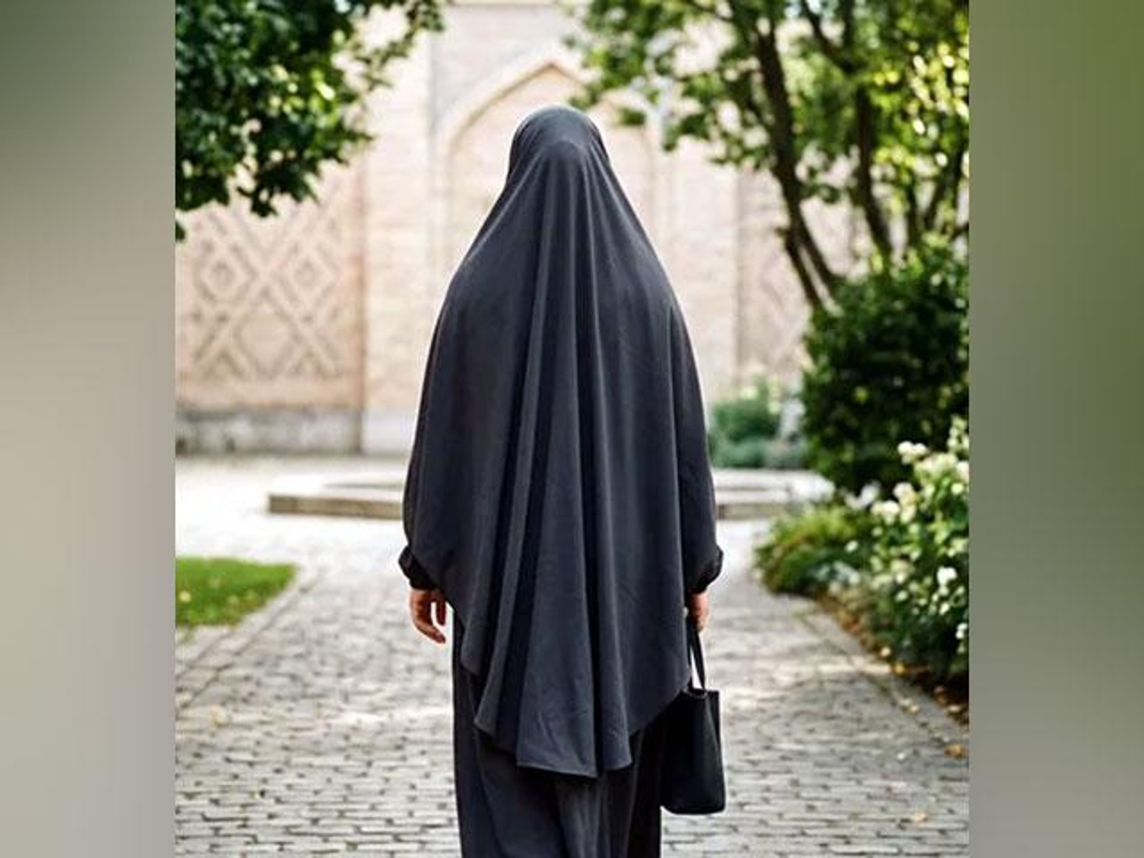 Back view of a person in a black full-body covering walking on a paved path.
