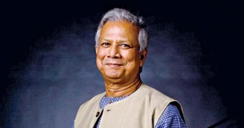 A smiling man with gray hair wearing a light tan vest over a blue patterned shirt.