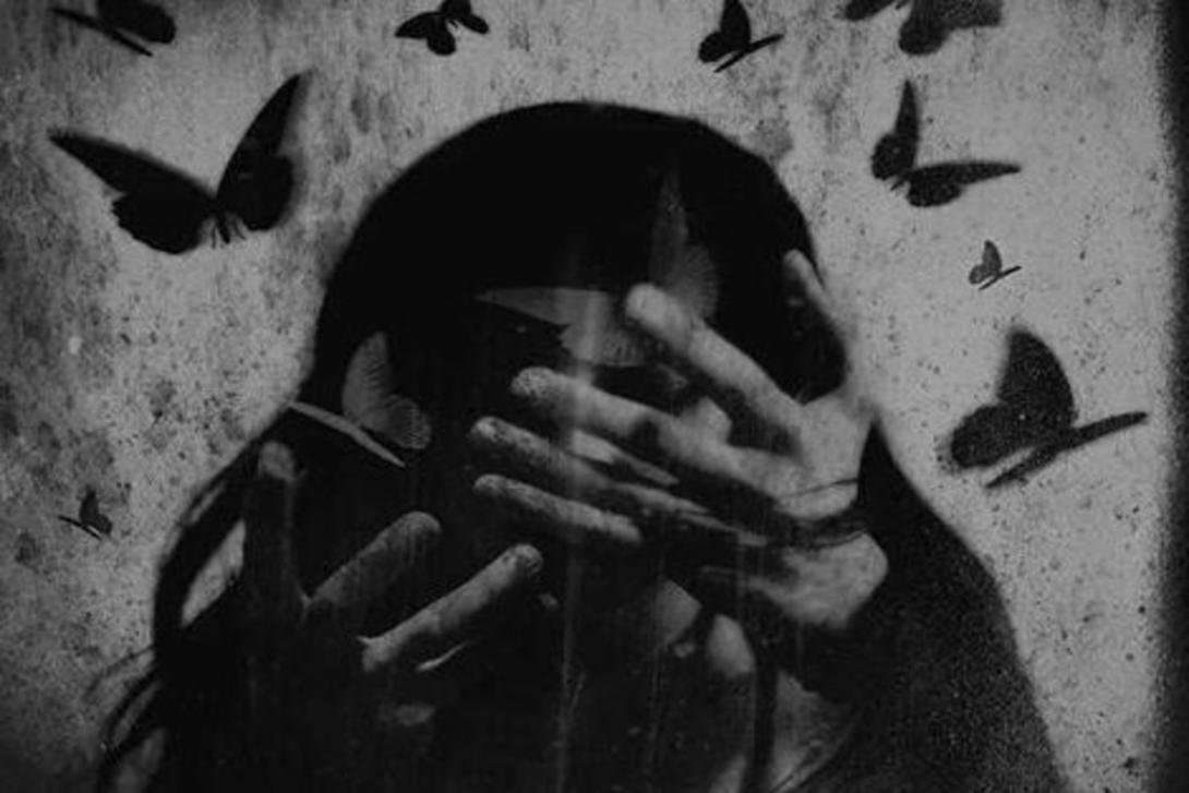 Gritty black and white image of a person with hands covering their eyes and forehead, surrounded by flying dark butterflies.
