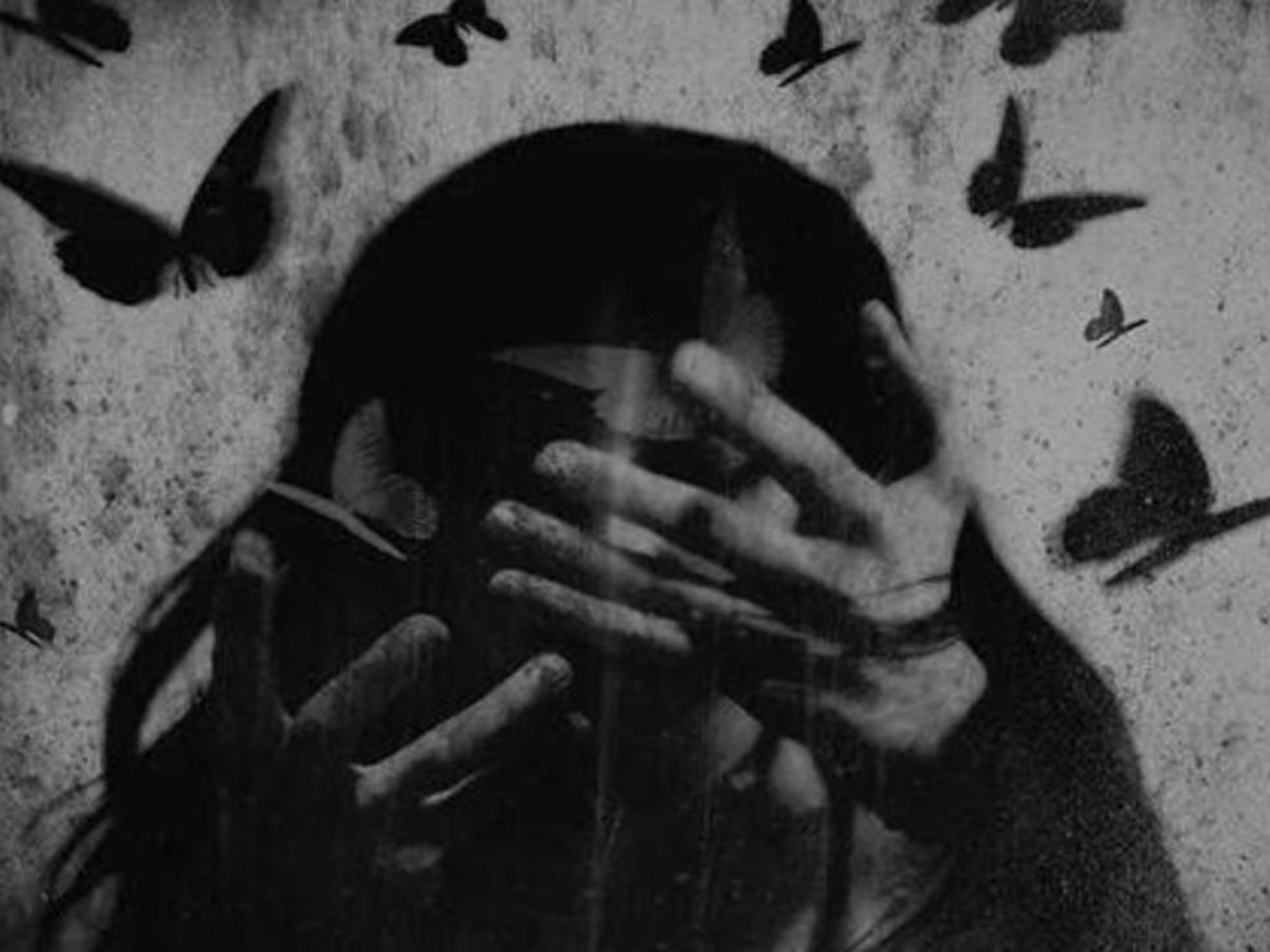 Gritty black and white image of a person with hands covering their eyes and forehead, surrounded by flying dark butterflies.