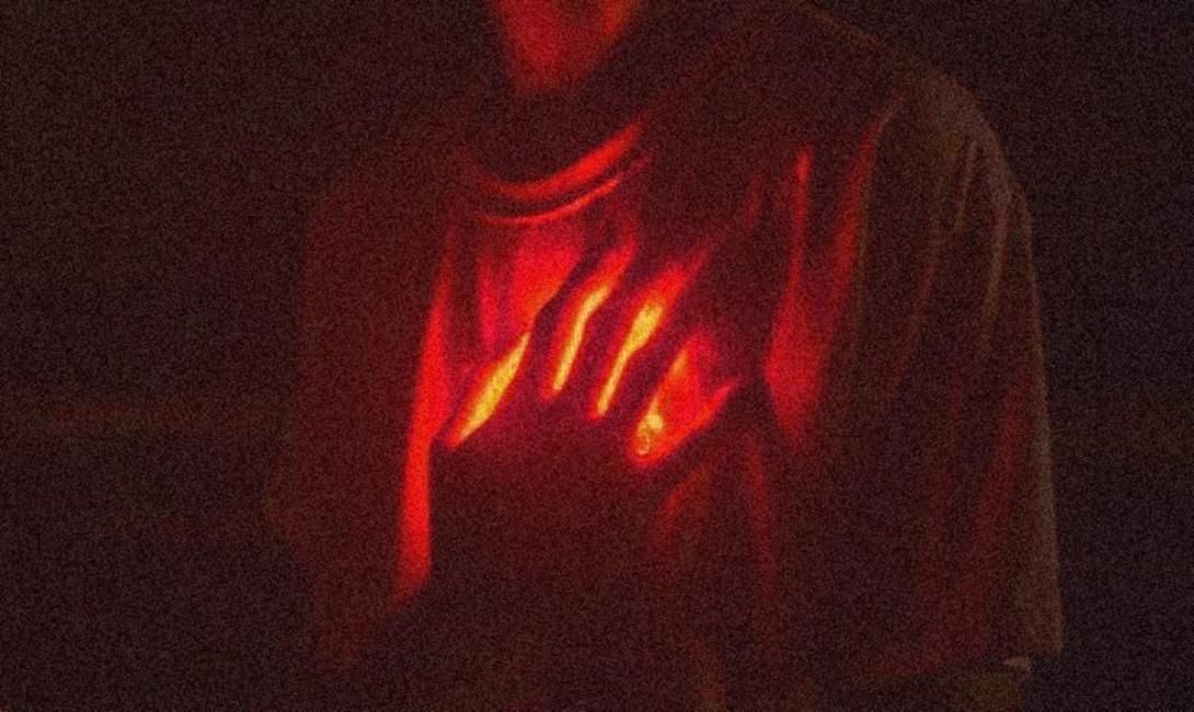 A person's chest glows red, with a hand illuminated in fiery yellow-orange light.
