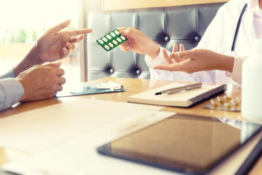 A doctor hands a blister pack of pills to a patient across a table.