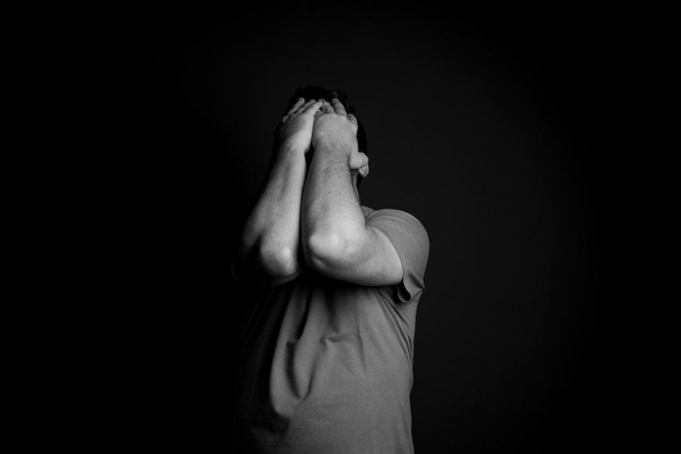 A person covers their face with their hands in black and white.