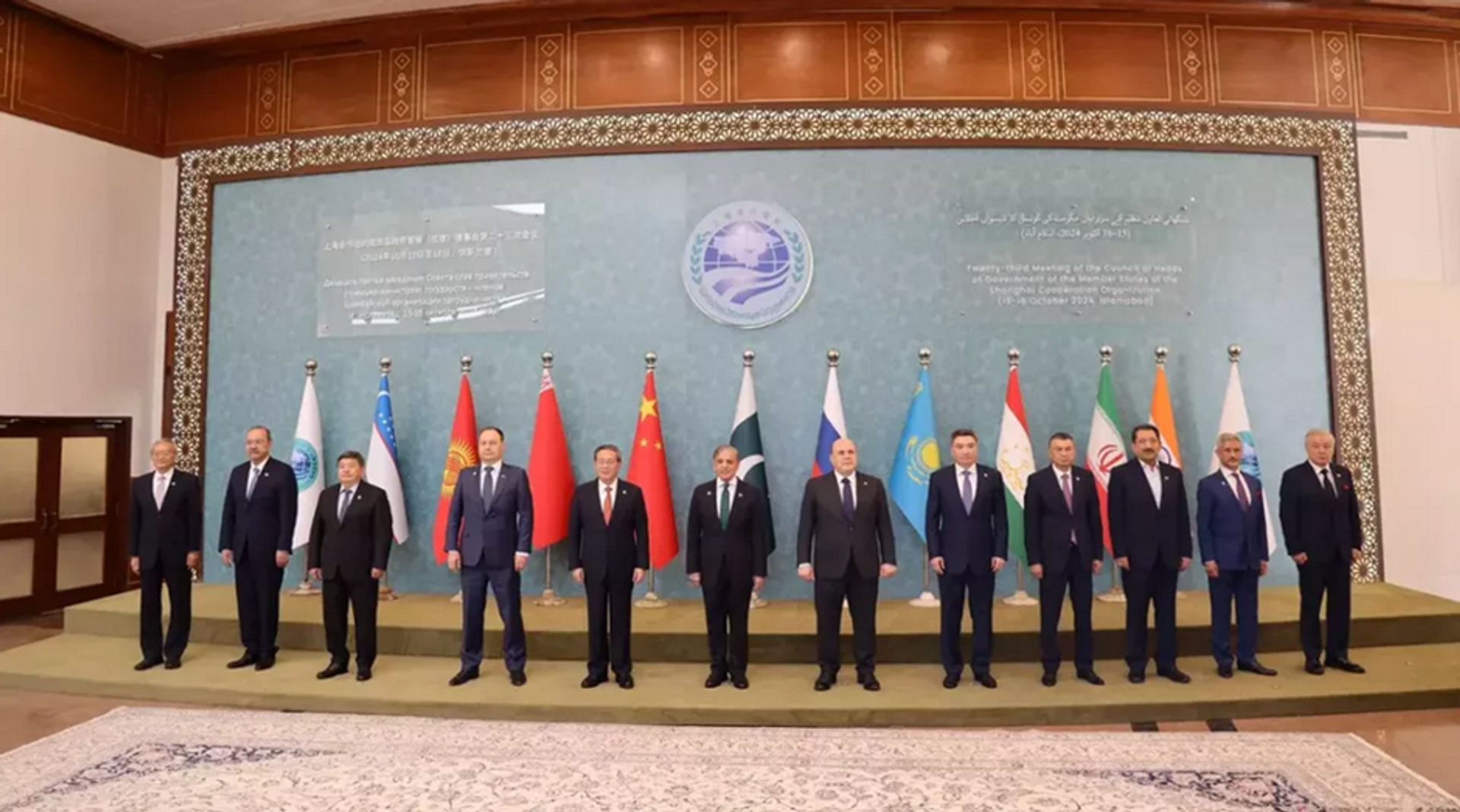 Twelve men in suits stand in a line in front of national flags and an ECO meeting backdrop.