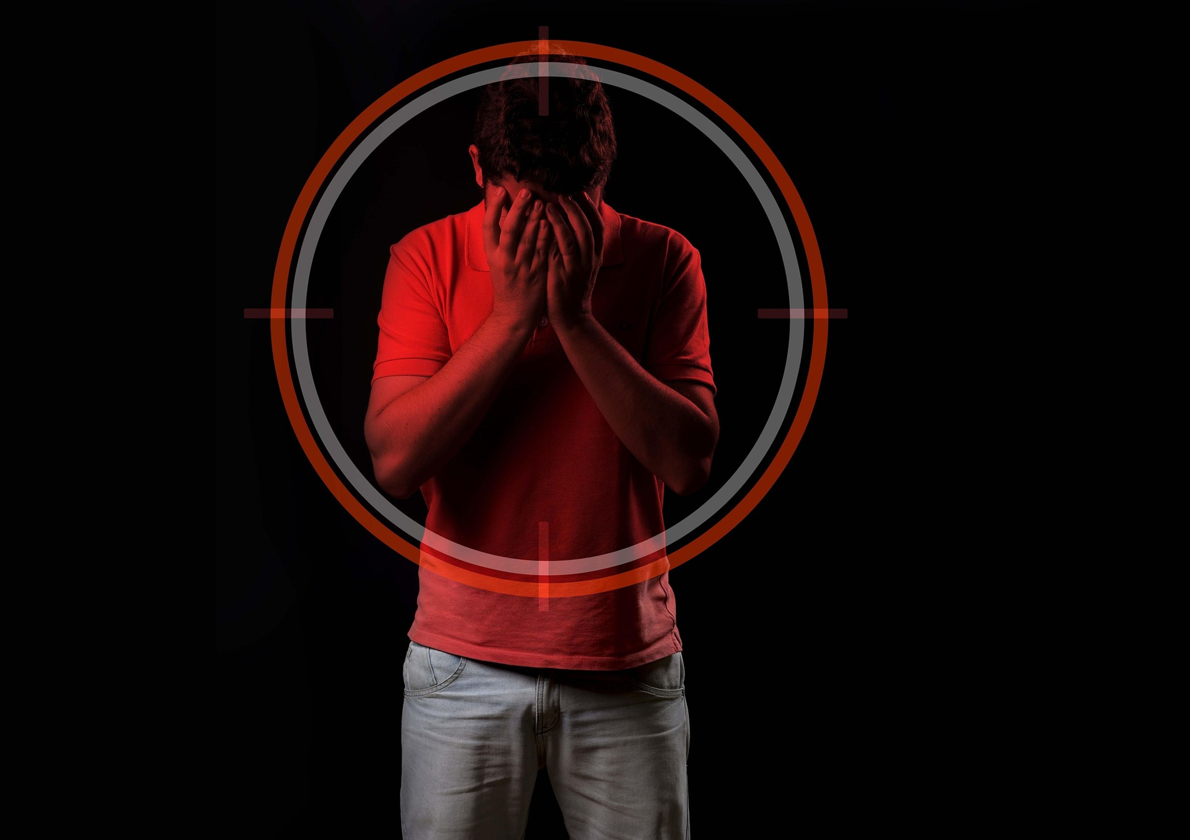 Red-lit person covering face, seen through a target scope.