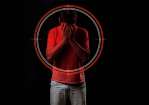 Red-lit person covering face, seen through a target scope.
