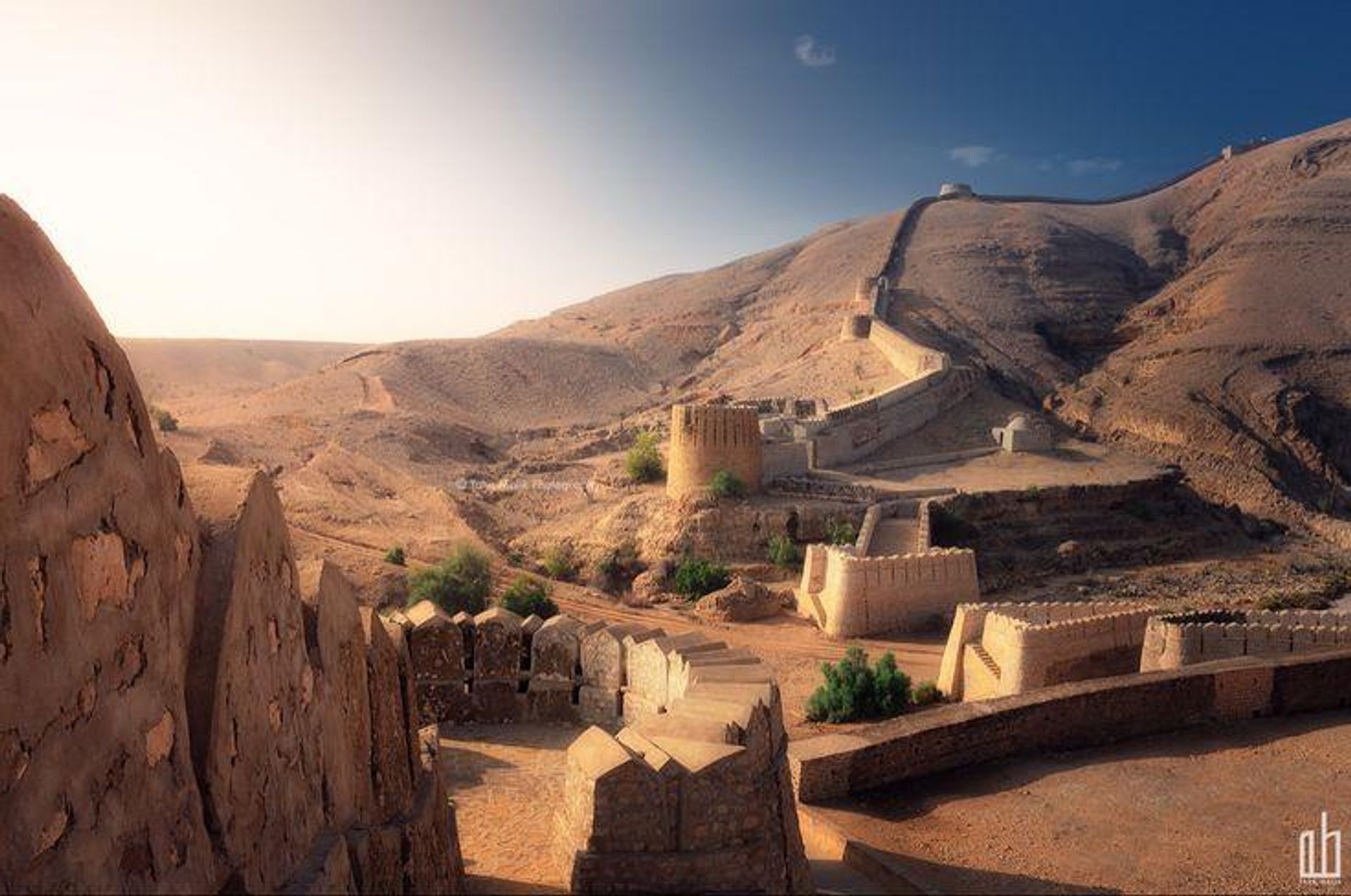 A long, winding fortress wall climbing a barren desert mountain at sunrise.
