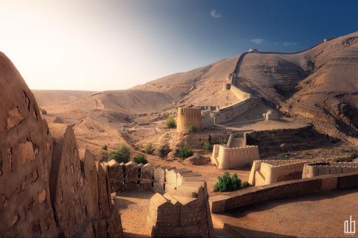 A long, winding fortress wall climbing a barren desert mountain at sunrise.