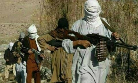 A group of masked men, armed with rifles and a machine gun, walk through a barren, outdoor area.