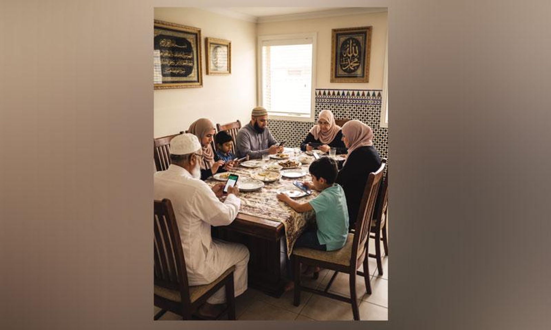 A multi-generational family sits at a dining table, with most members looking at their smartphones.
