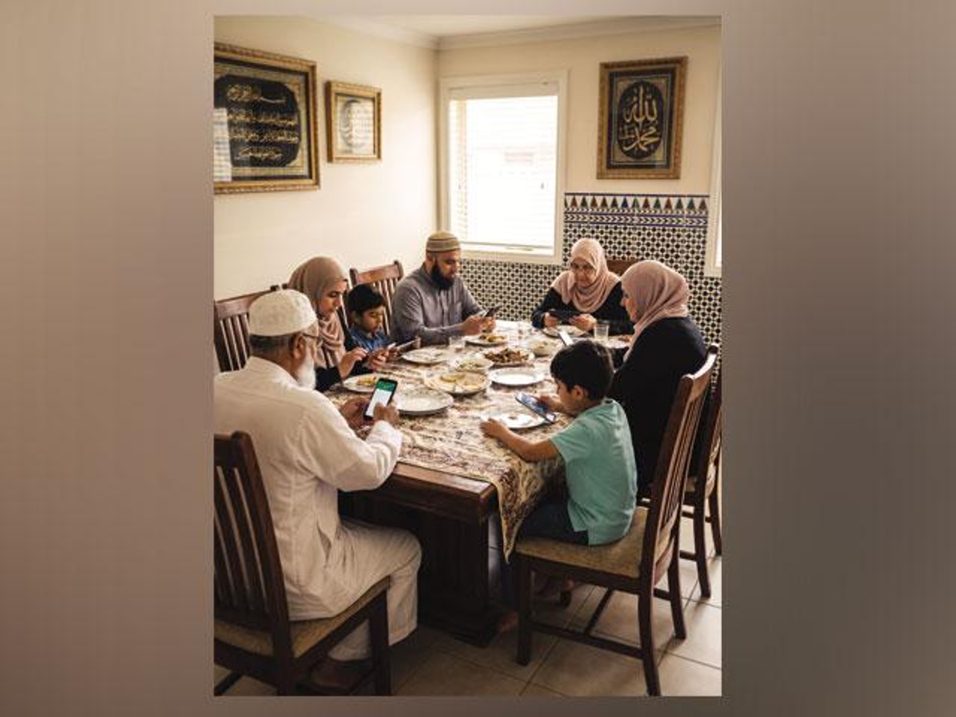 A multi-generational family sits at a dining table, with most members looking at their smartphones.