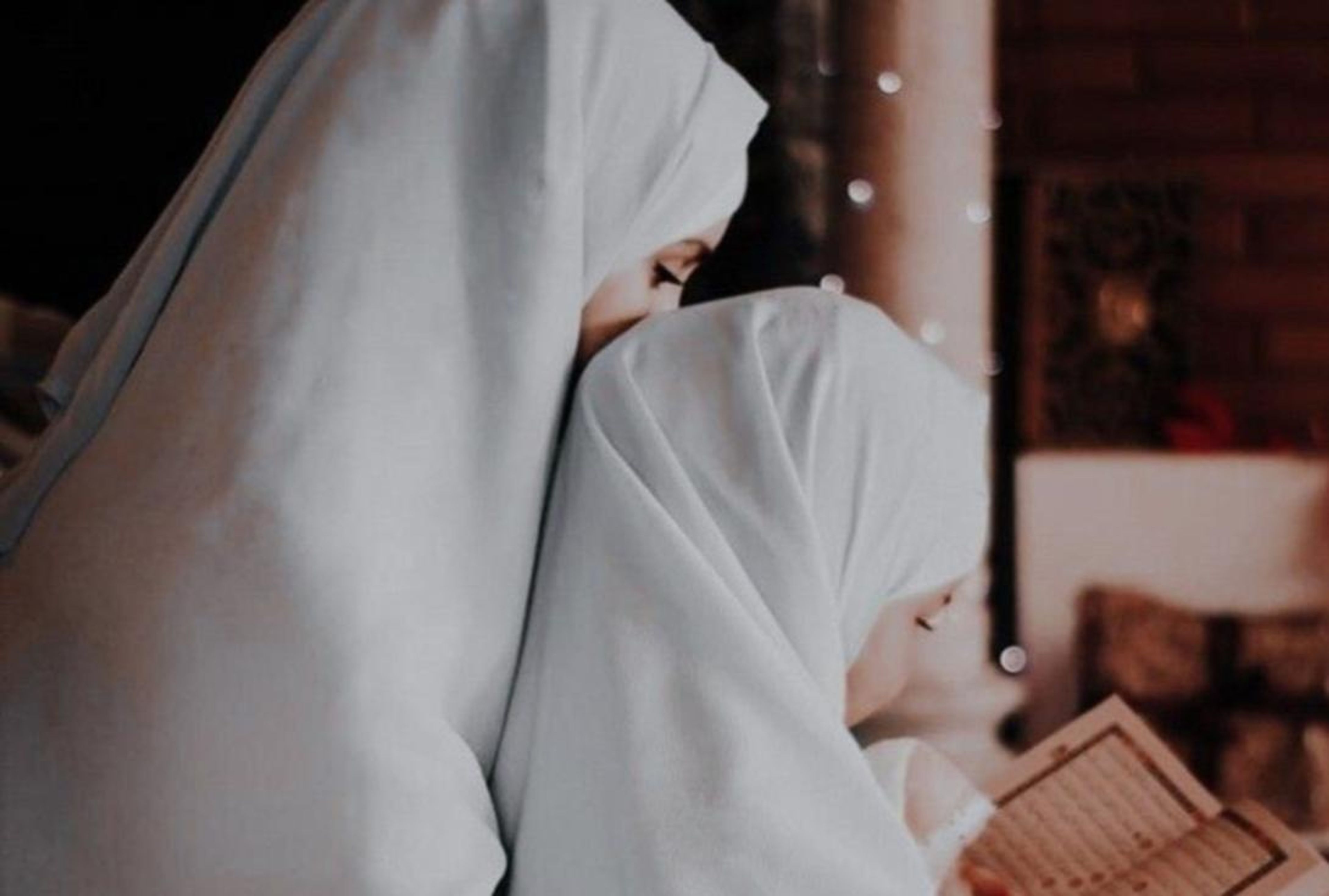 A woman and child wearing white hijabs read a book together.