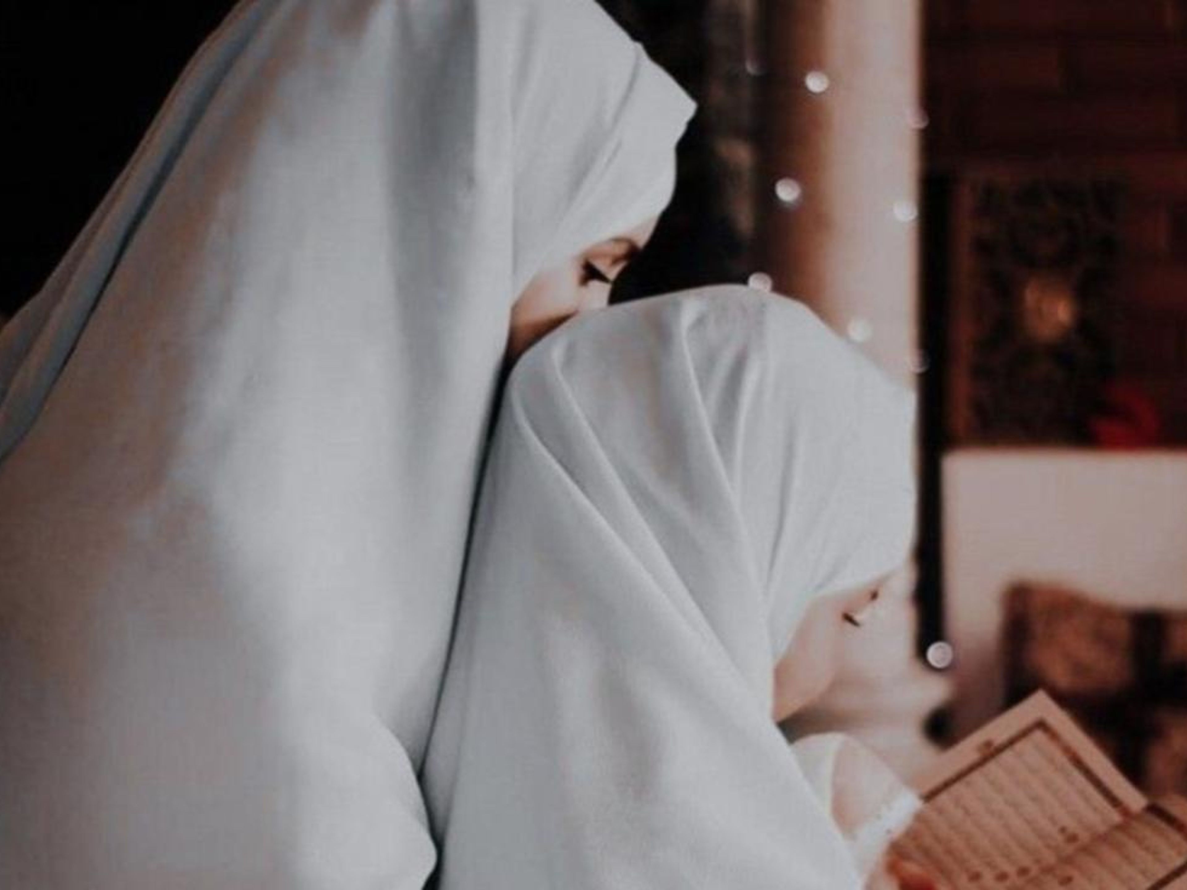 A woman and child wearing white hijabs read a book together.