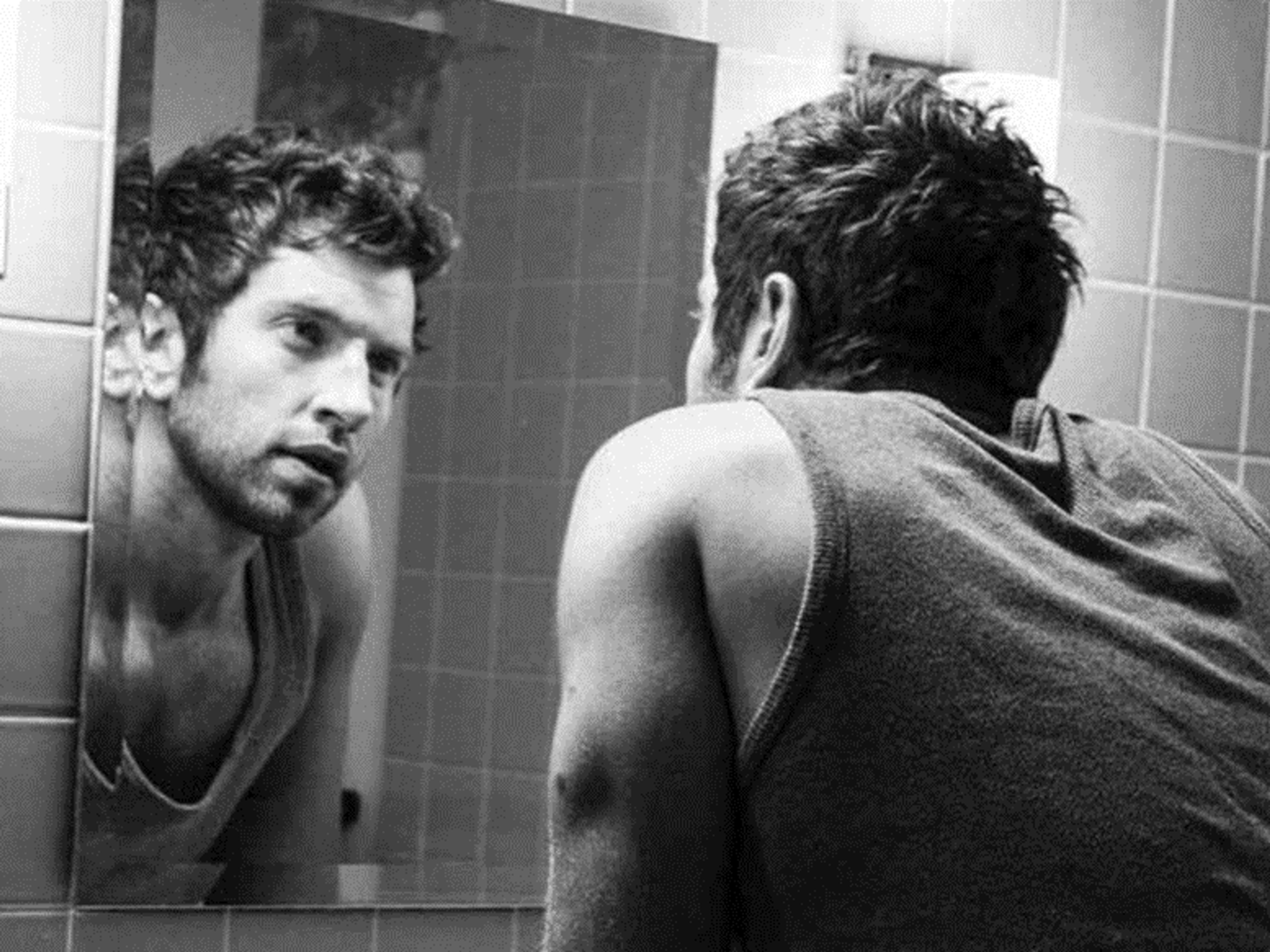 Black and white image of a man looking at his reflection in a mirror.