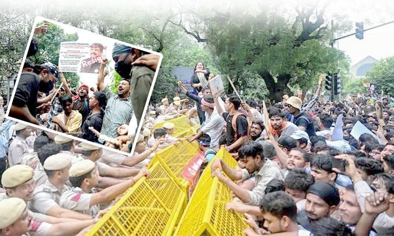 A large crowd of protestors pushes against yellow police barricades, confronting police officers, with some holding "Resign" signs.
