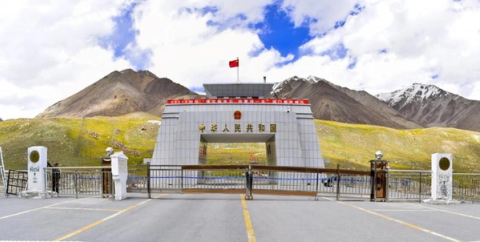 Chinese border gate with a flag, mountains, and a road barrier.