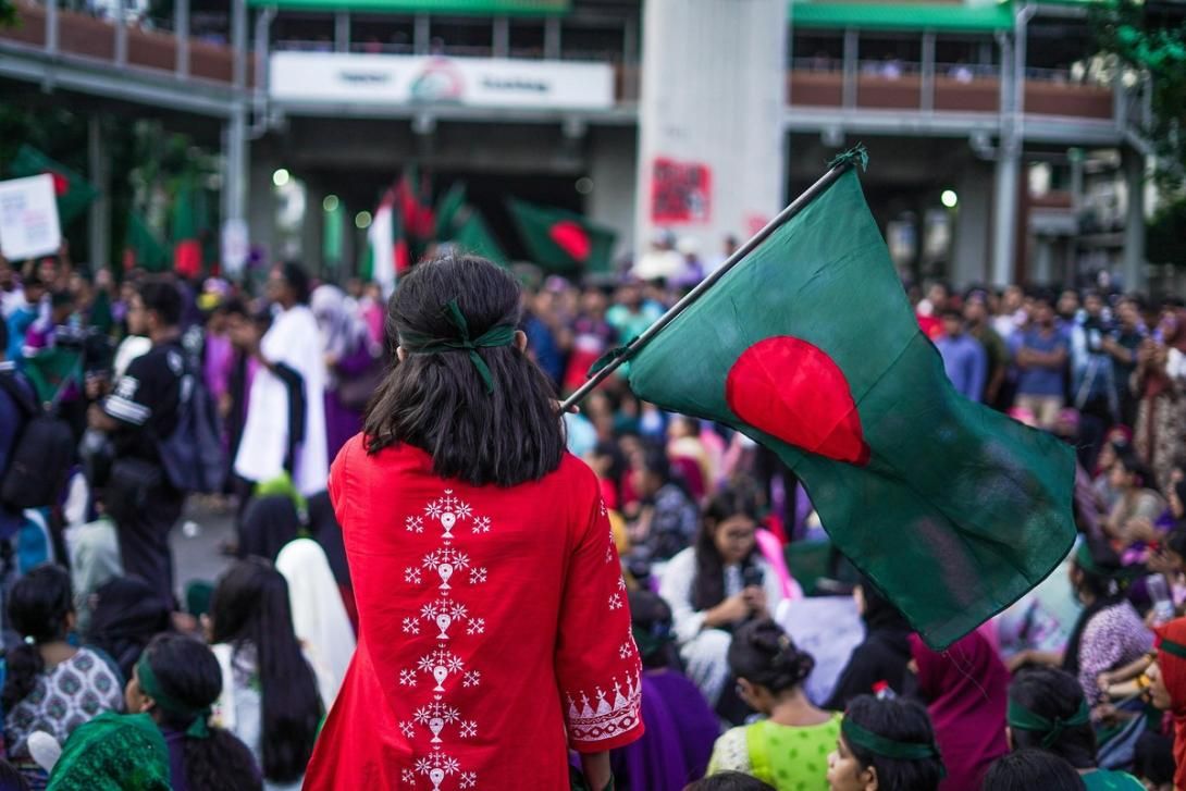 A person from behind holds a Bangladesh flag in a crowd.