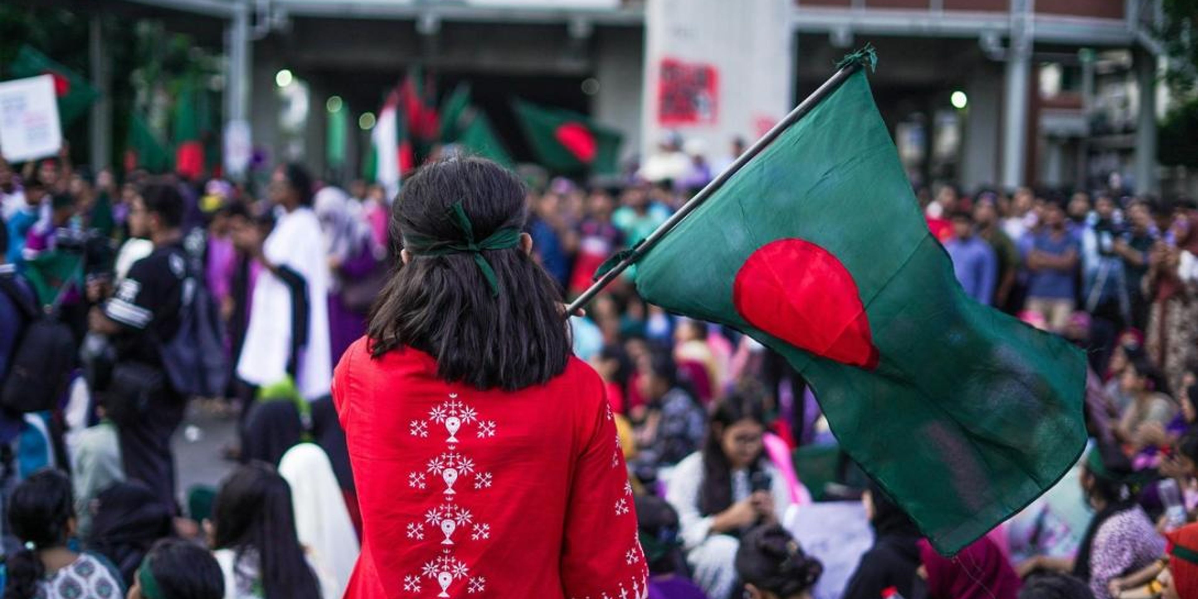 A person from behind holds a Bangladesh flag in a crowd.