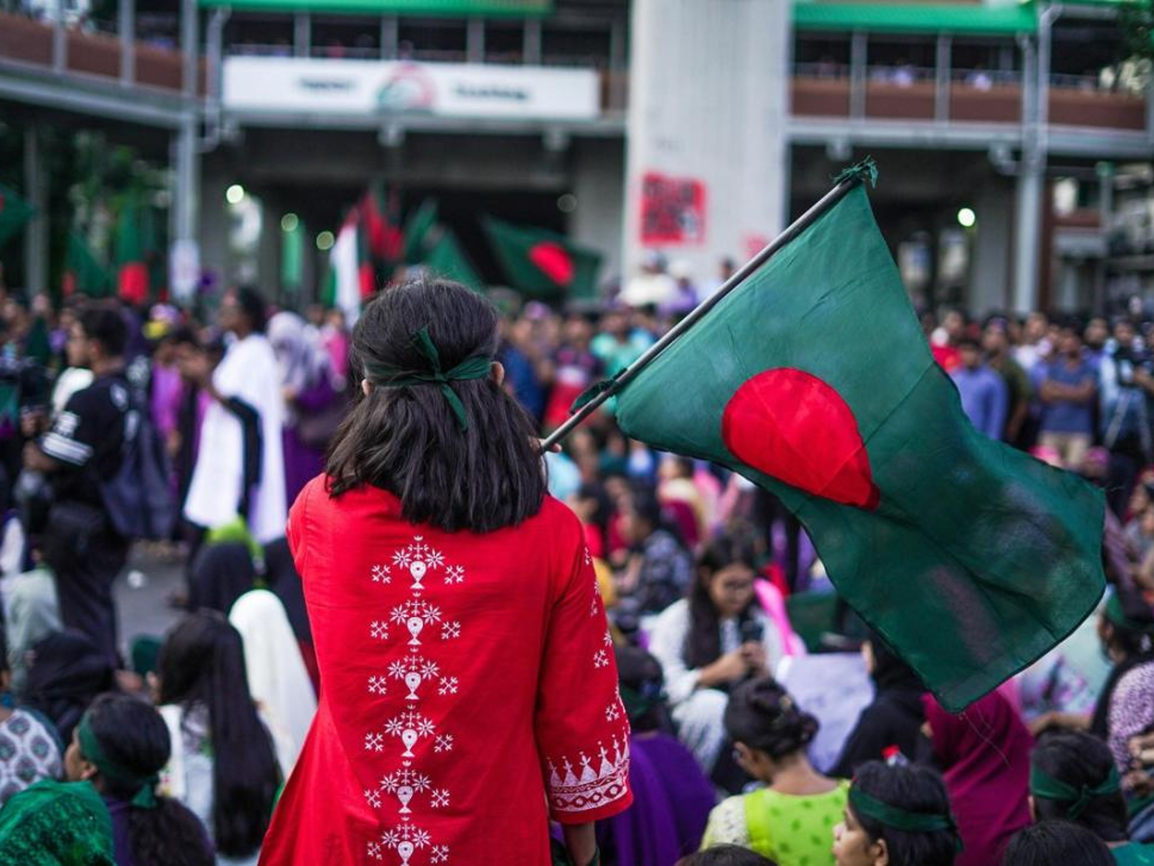 A person from behind holds a Bangladesh flag in a crowd.