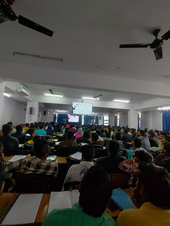 Students in a large lecture hall watch a presentation on a screen.