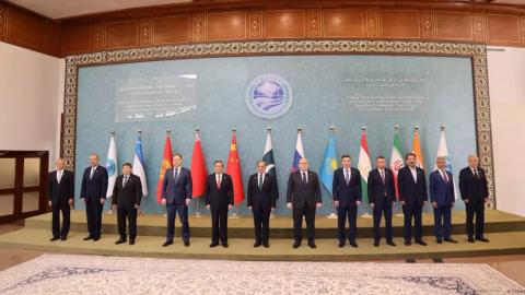 Group photo of thirteen men in suits standing before a row of national and organizational flags.