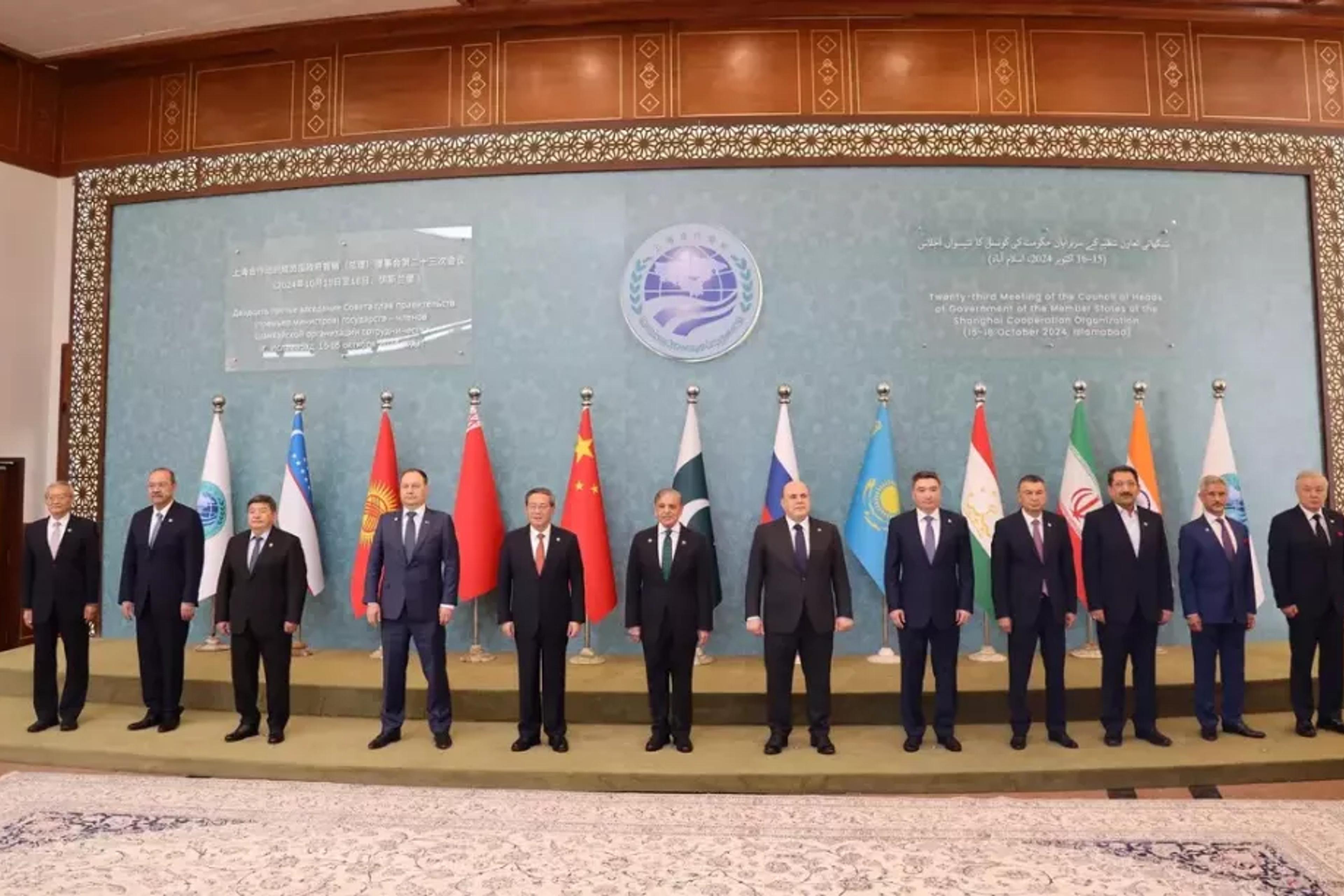 Group photo of thirteen men in suits standing before a row of national and organizational flags.