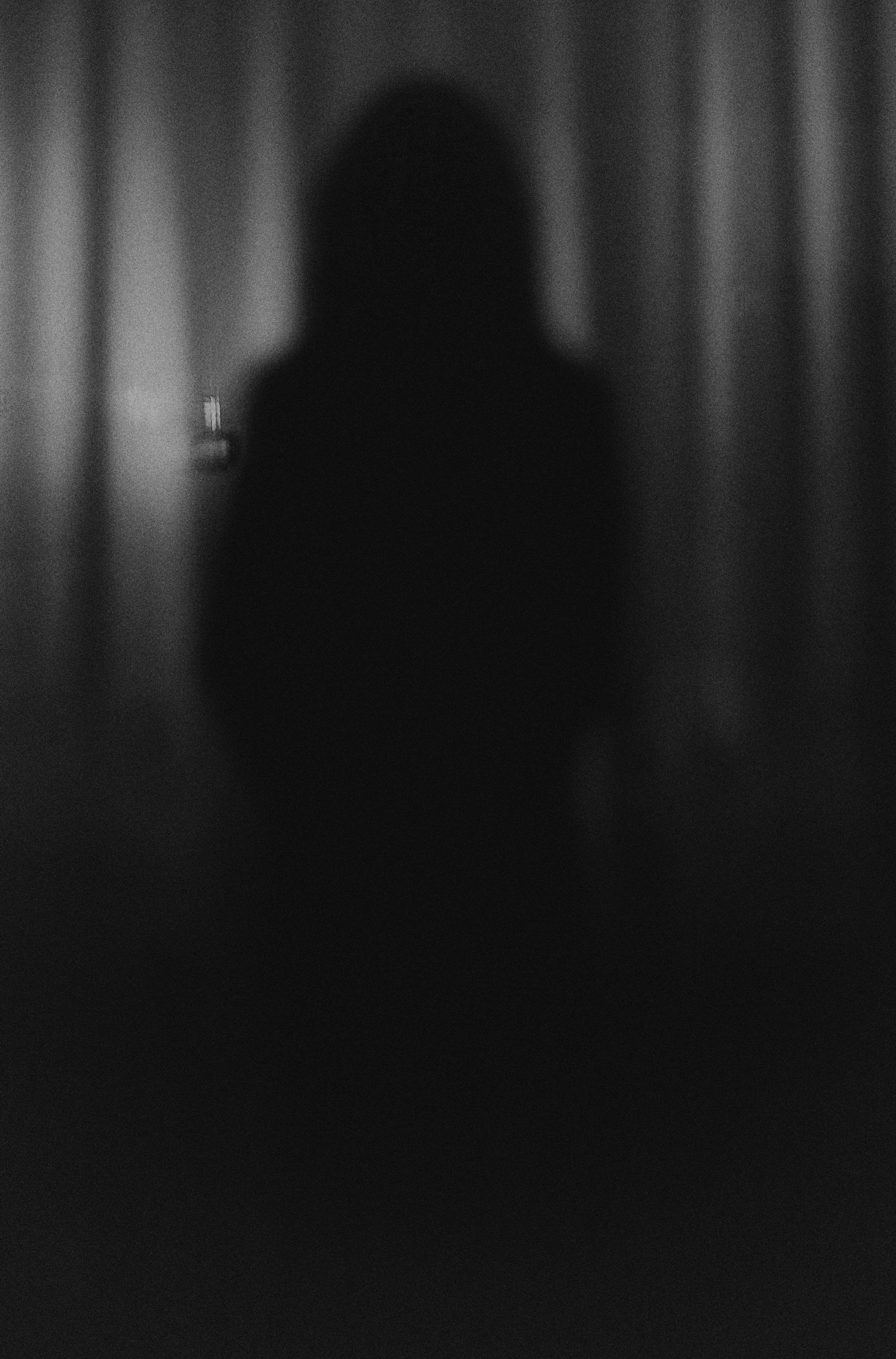 Dark, blurry silhouette of a person against a textured background in black and white.