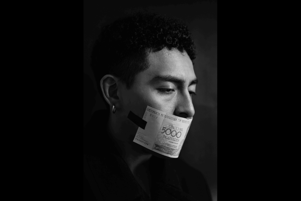 Black and white portrait of a person with a 5000 Bolivares banknote taped over their mouth, looking down.