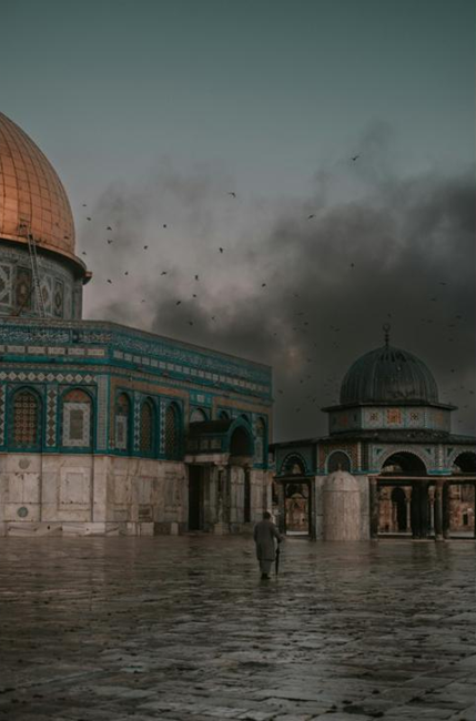 The golden-domed Dome of the Rock and another historic building under a dark, bird-filled sky, with a lone figure walking on wet ground.