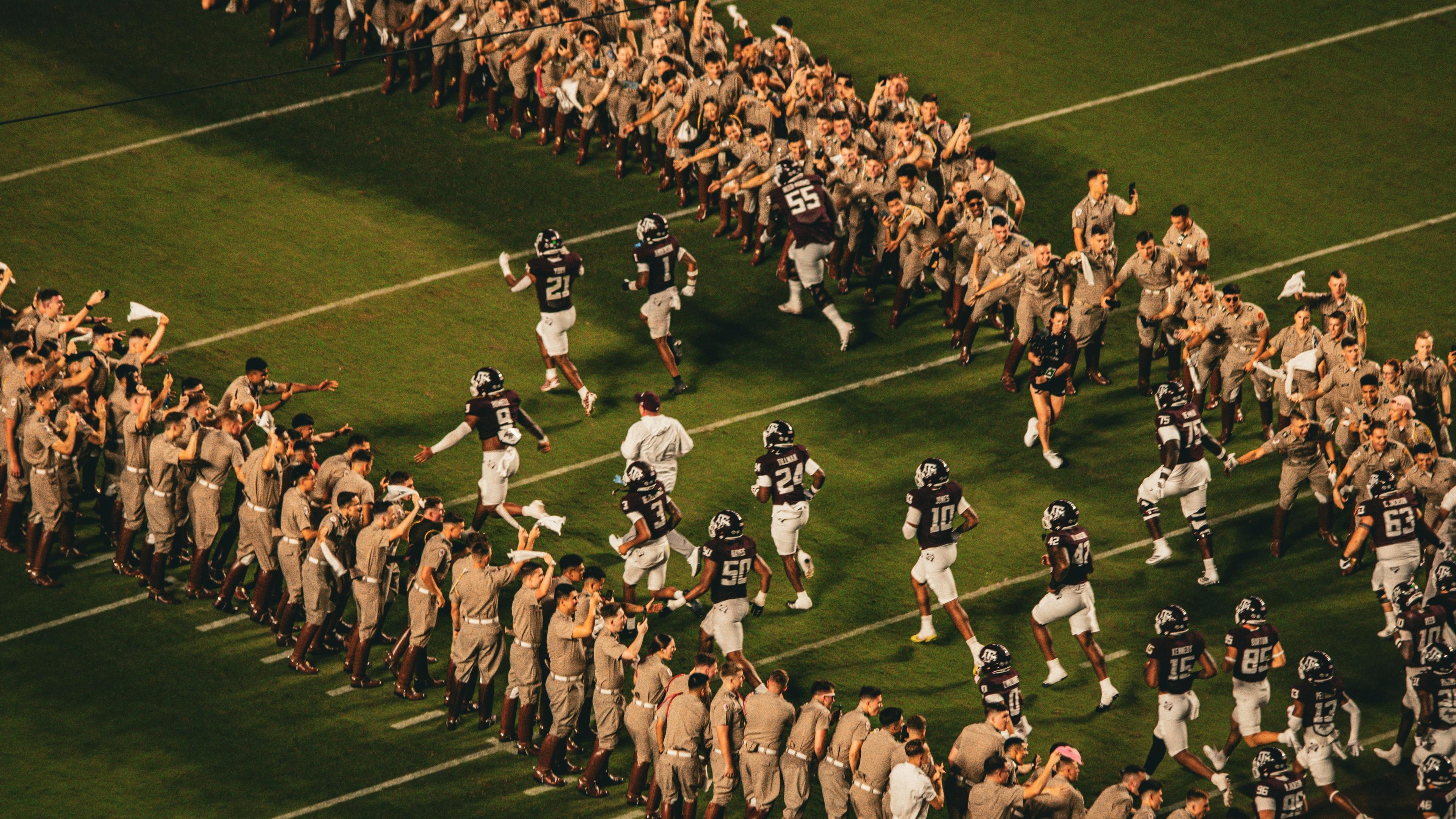 Football players run onto the field between cheering crowds