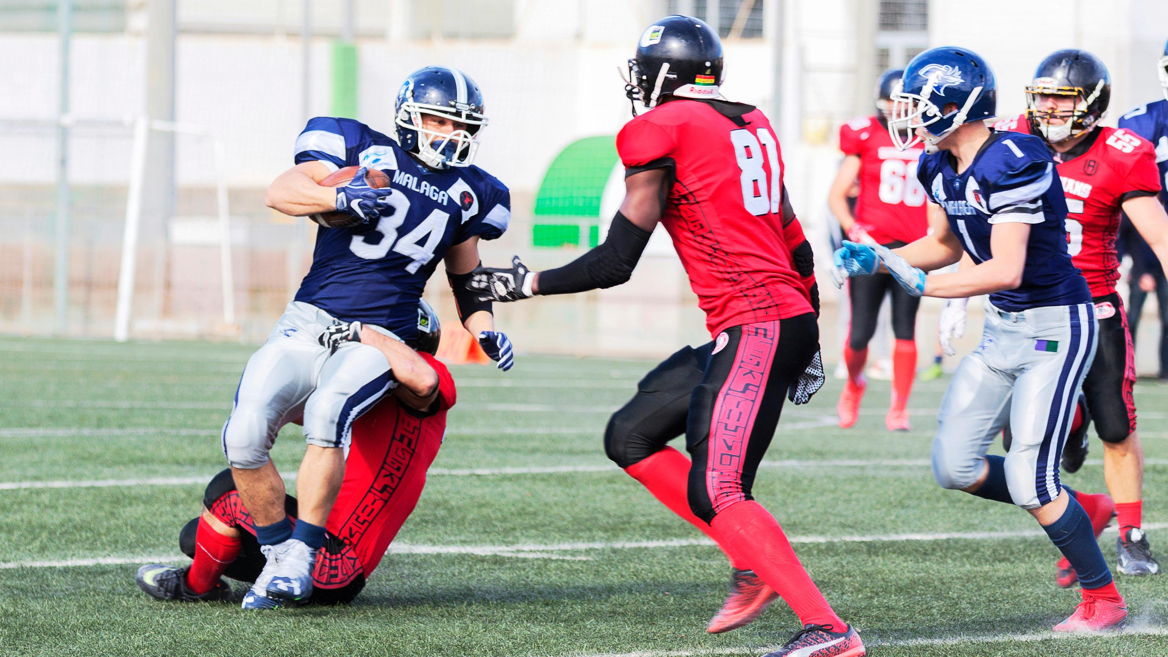 Football players in red jersey shirt and red pants running on green grass field during daytime