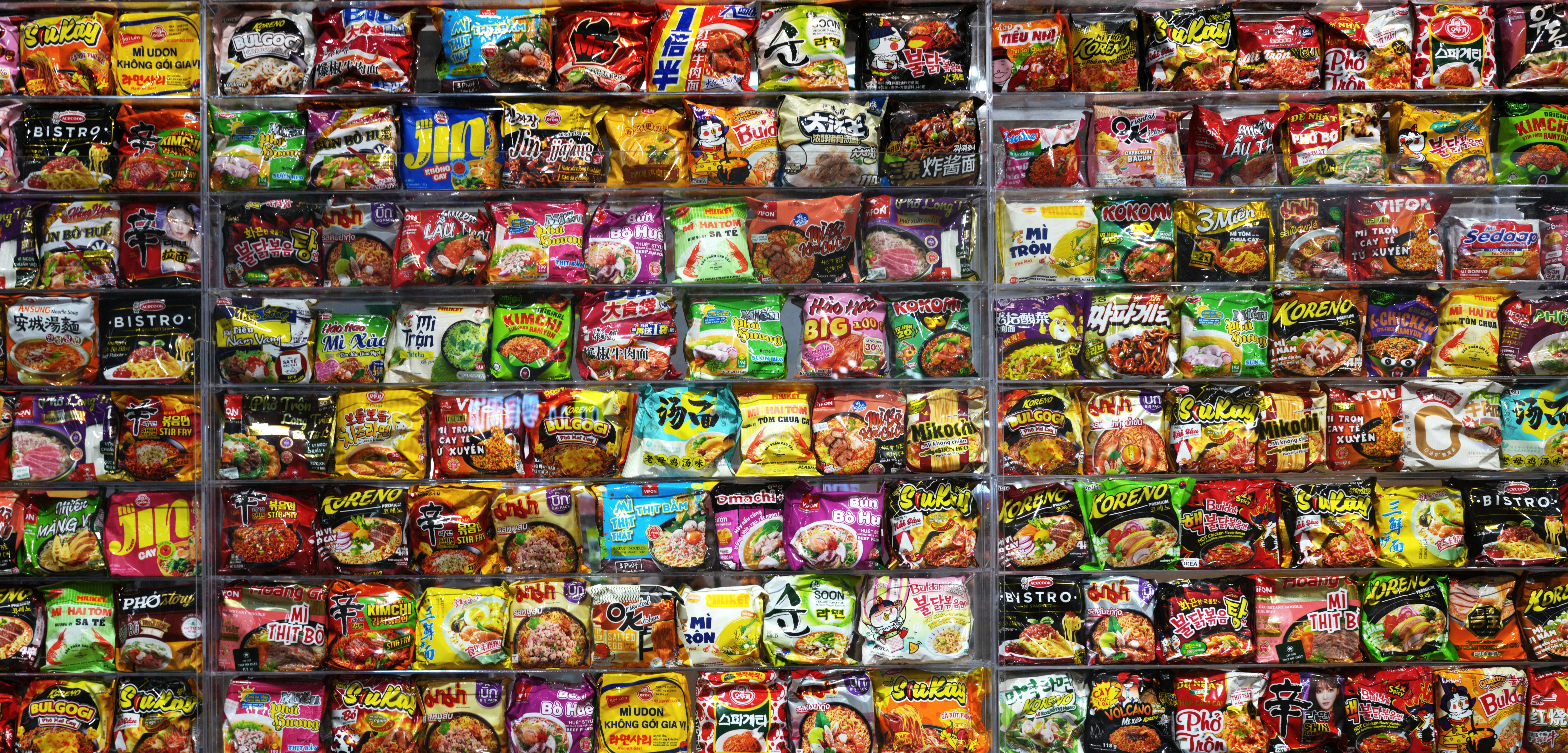 A large display of colorful instant noodle packages arranged on shelves in a store